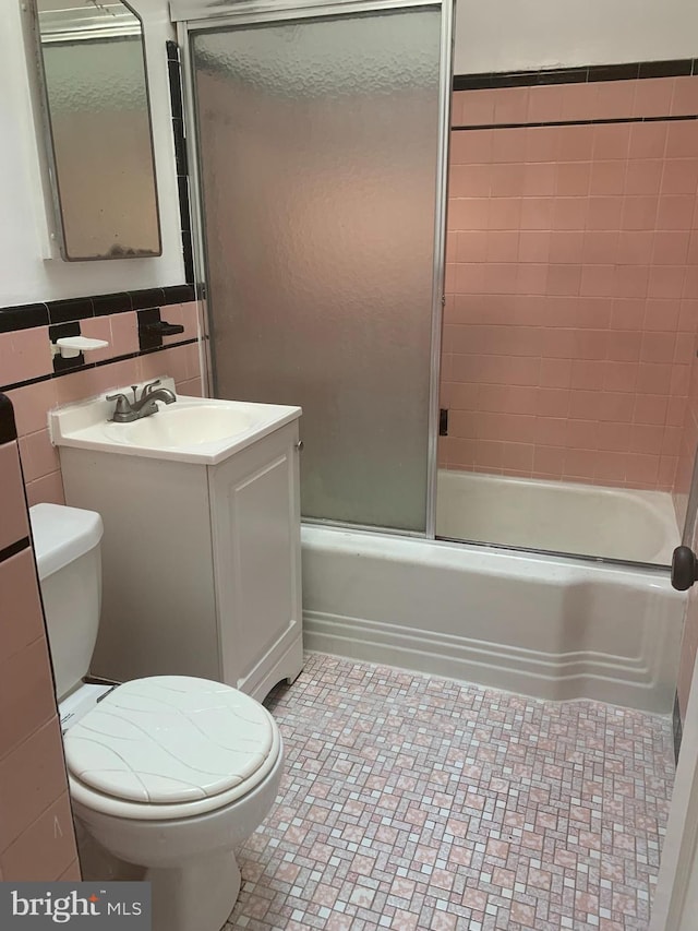 bathroom with vanity, shower / bath combination with glass door, wainscoting, tile walls, and toilet