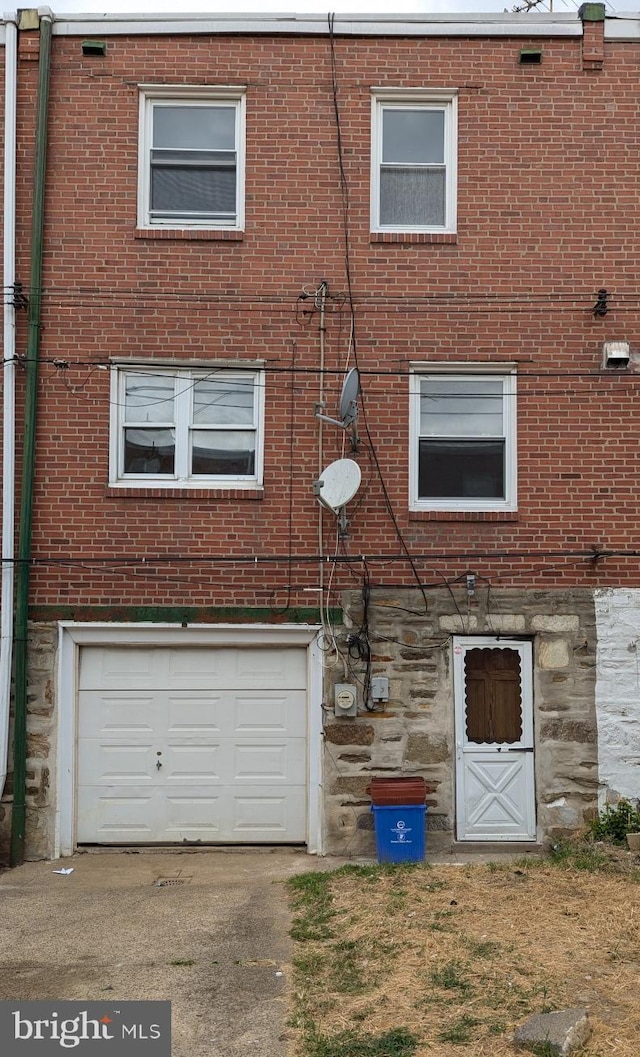 rear view of property featuring brick siding, stone siding, and a garage