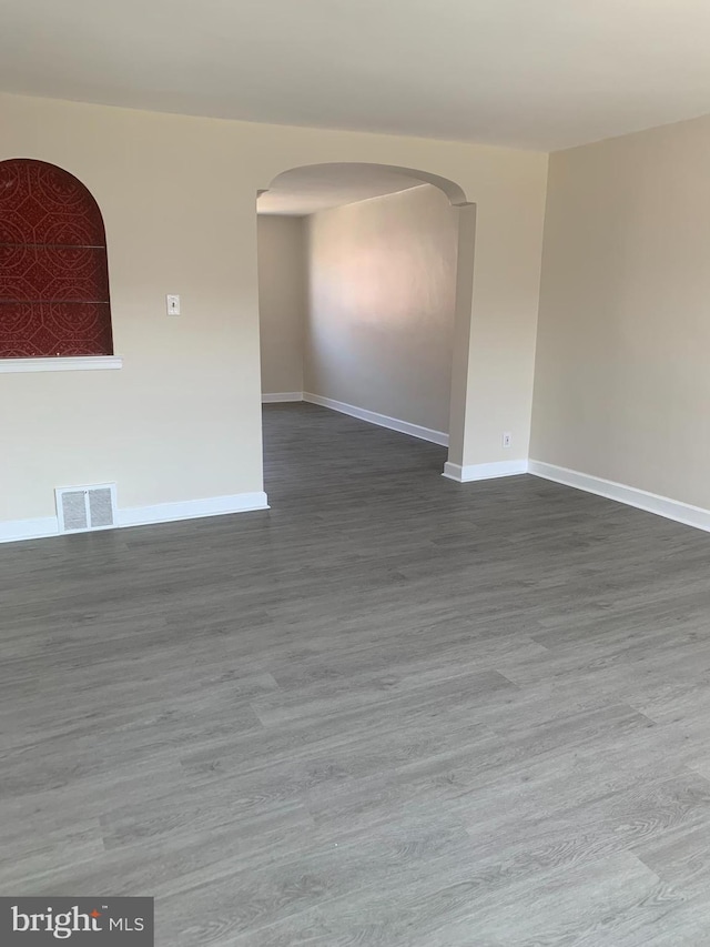 unfurnished room featuring arched walkways, visible vents, baseboards, and wood finished floors