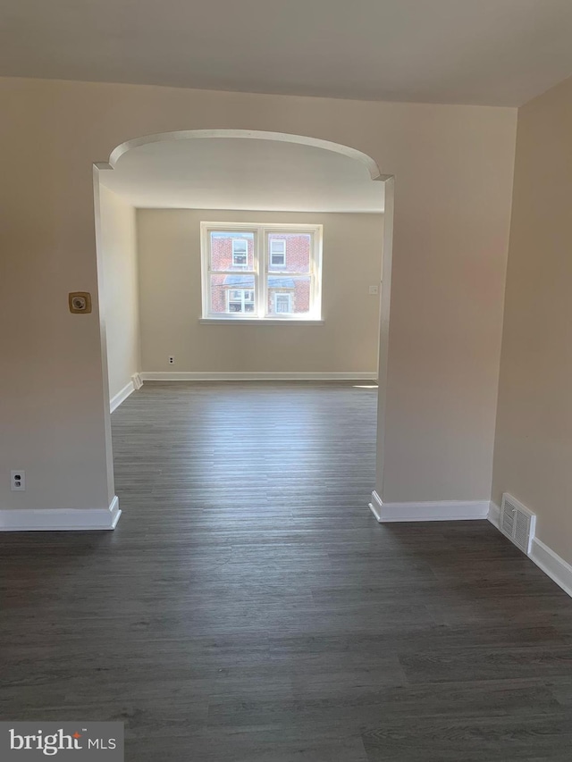 spare room featuring arched walkways, visible vents, baseboards, and dark wood-style flooring