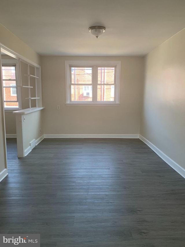 spare room featuring dark wood finished floors, plenty of natural light, and baseboards