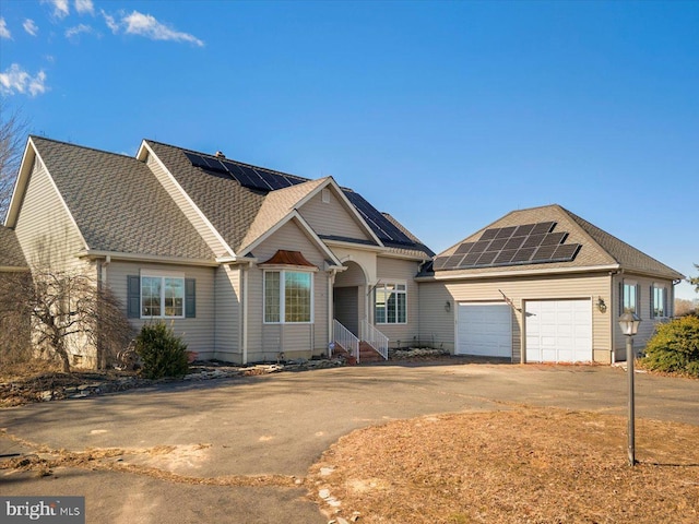 view of front of home featuring roof mounted solar panels, a garage, driveway, and roof with shingles