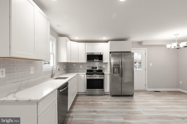 kitchen with decorative backsplash, appliances with stainless steel finishes, a notable chandelier, white cabinets, and a sink