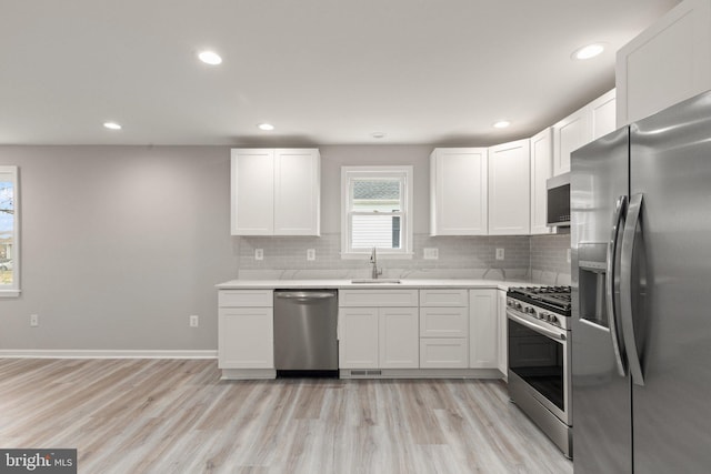 kitchen with a sink, light countertops, light wood-style floors, appliances with stainless steel finishes, and tasteful backsplash