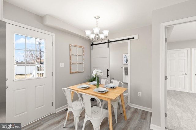 dining area featuring a chandelier, light wood finished floors, baseboards, and a barn door