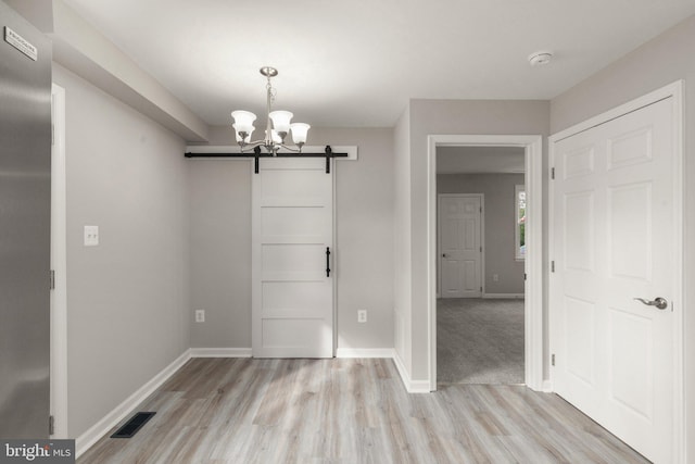 unfurnished dining area with visible vents, baseboards, light wood-type flooring, a barn door, and an inviting chandelier