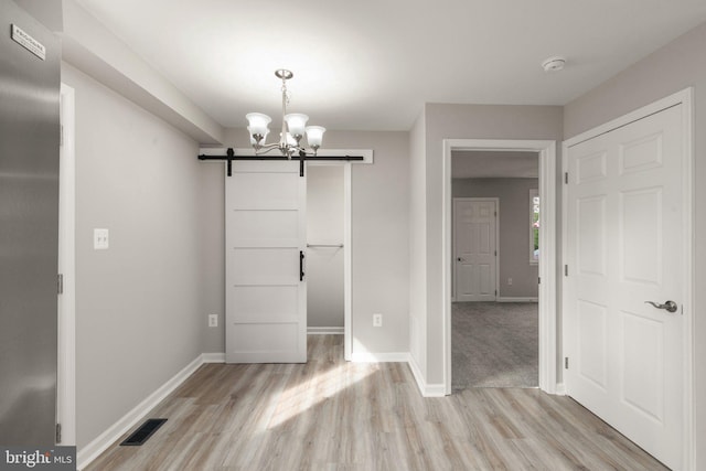 unfurnished dining area featuring baseboards, visible vents, light wood-style flooring, a barn door, and a chandelier