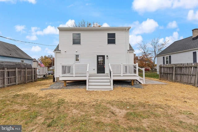 rear view of property featuring a wooden deck, a lawn, and fence