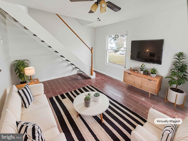 living area featuring stairway, a ceiling fan, and baseboards