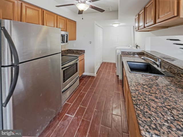 kitchen featuring a sink, appliances with stainless steel finishes, brown cabinetry, washer / dryer, and wood tiled floor