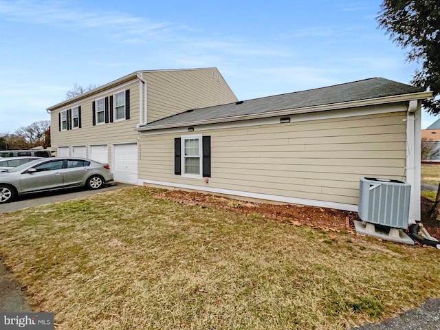 view of home's exterior with central AC unit, a garage, driveway, and a lawn