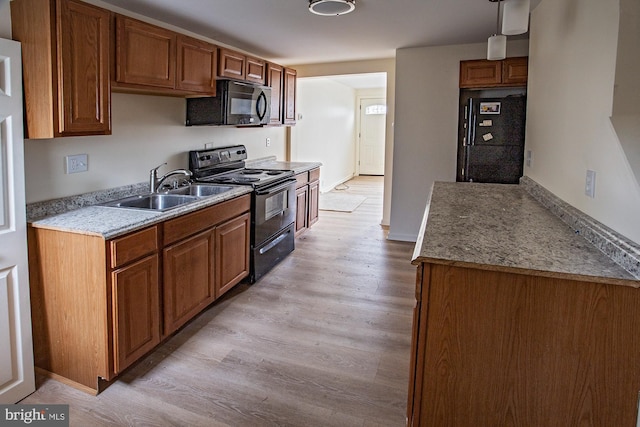 kitchen featuring light countertops, light wood-style flooring, brown cabinets, black appliances, and a sink