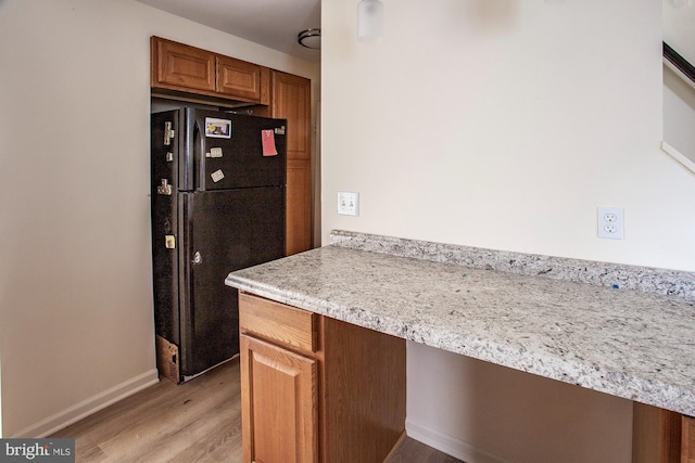 kitchen featuring brown cabinetry, baseboards, light wood-style flooring, freestanding refrigerator, and light countertops