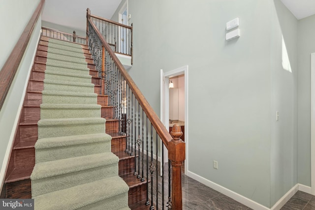 stairway with wood finished floors, baseboards, and a towering ceiling