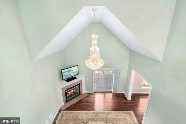 interior space with baseboards, a chandelier, wood finished floors, a glass covered fireplace, and high vaulted ceiling