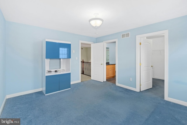 unfurnished bedroom featuring visible vents, ensuite bath, dark colored carpet, baseboards, and a spacious closet