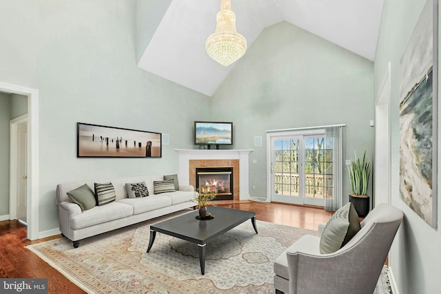 living room with baseboards, wood finished floors, a tile fireplace, and high vaulted ceiling