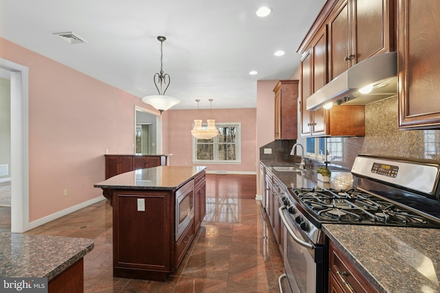 kitchen featuring a sink, decorative backsplash, under cabinet range hood, appliances with stainless steel finishes, and a center island