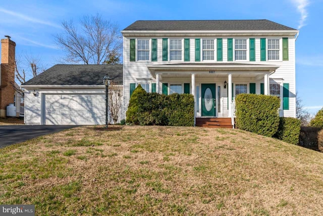 colonial inspired home with a garage, a porch, a front lawn, and aphalt driveway