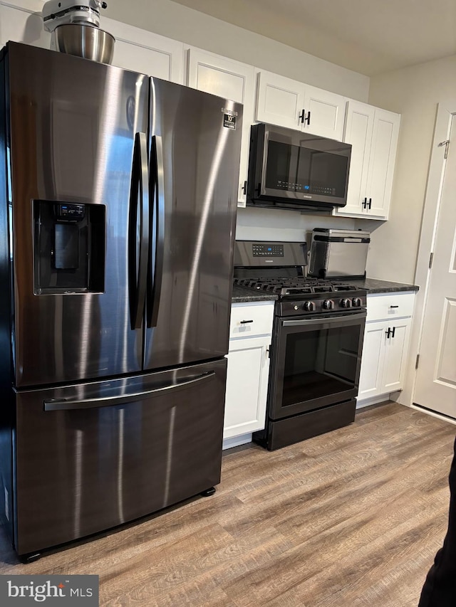 kitchen with stainless steel appliances, dark countertops, wood finished floors, and white cabinets