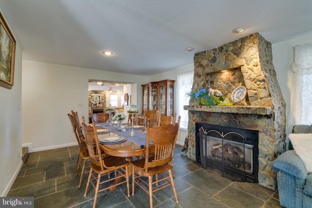 dining area featuring baseboards, a textured ceiling, stone tile flooring, and a fireplace