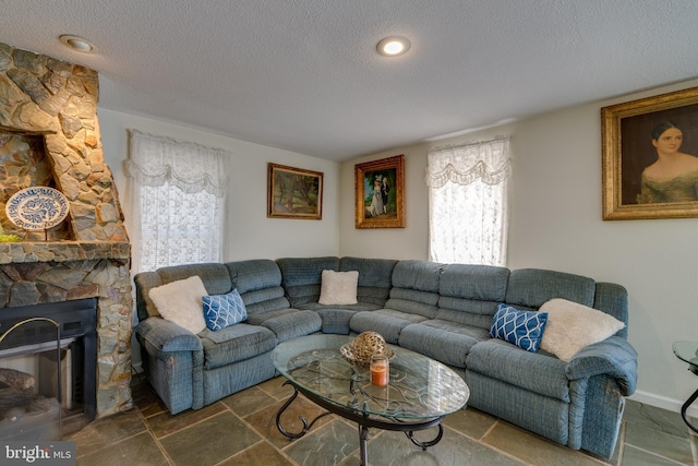 living room with stone tile flooring, a fireplace, baseboards, and a textured ceiling