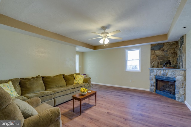 living room with baseboards, a fireplace, wood finished floors, a textured ceiling, and a ceiling fan