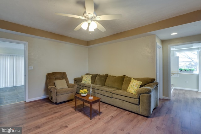 living area with light wood-style flooring, a ceiling fan, and baseboards