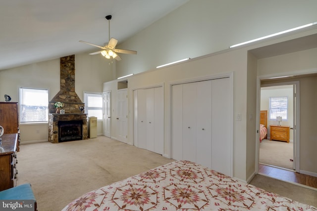 bedroom with a stone fireplace, multiple closets, carpet floors, and high vaulted ceiling