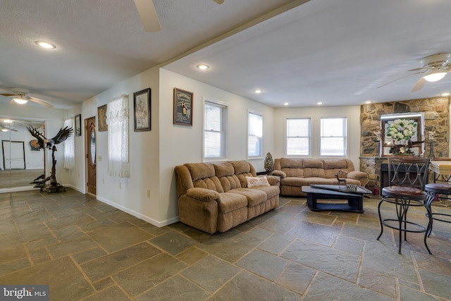 living area featuring stone tile flooring, baseboards, and ceiling fan