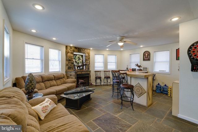 living room featuring a stone fireplace, plenty of natural light, stone tile floors, and ceiling fan