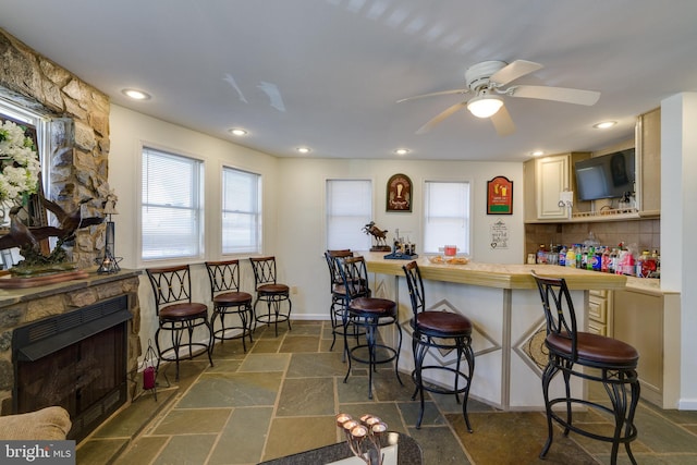 kitchen featuring stone tile floors, backsplash, a kitchen breakfast bar, and ceiling fan