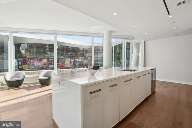 kitchen with visible vents, a center island with sink, wood finished floors, white cabinetry, and a sink