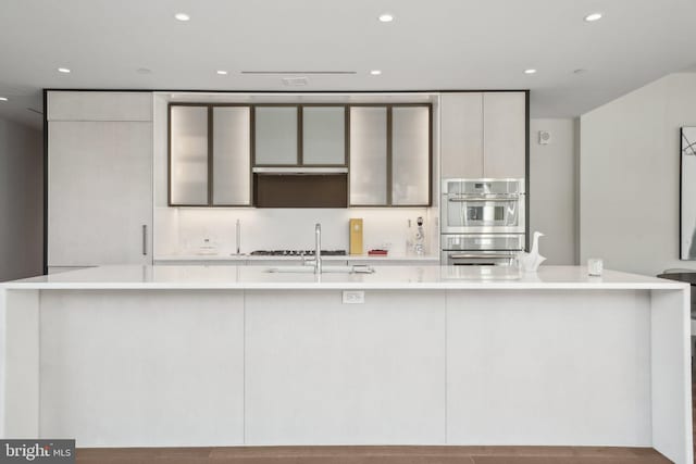 kitchen with modern cabinets, a sink, stainless steel double oven, light countertops, and a large island with sink