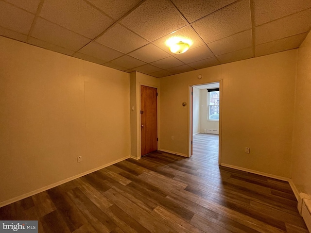 unfurnished room featuring dark wood finished floors, baseboard heating, baseboards, and a drop ceiling