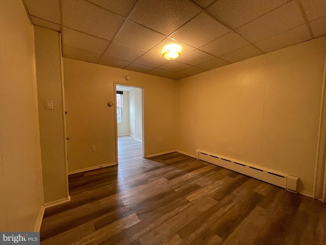 spare room with a drop ceiling, a baseboard radiator, baseboards, and wood finished floors