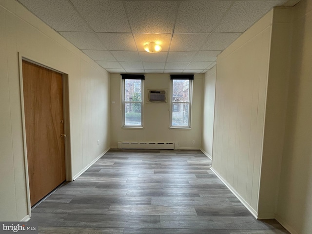 interior space featuring baseboards, a paneled ceiling, wood finished floors, a wall mounted AC, and a baseboard radiator