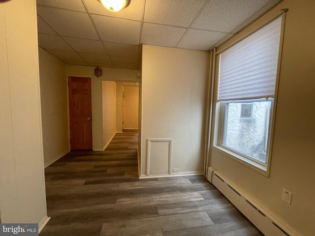 empty room featuring wood finished floors, baseboards, a drop ceiling, and a baseboard radiator