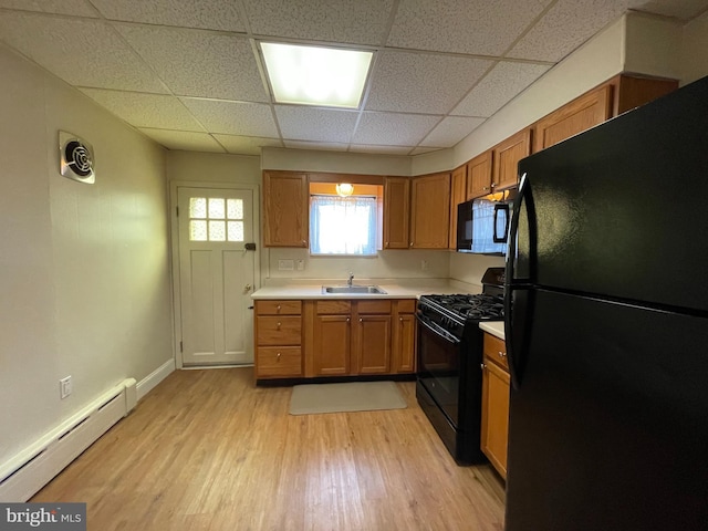 kitchen featuring light wood finished floors, baseboard heating, brown cabinetry, black appliances, and a sink