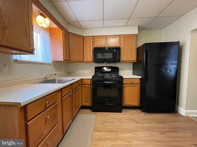 kitchen with light countertops, brown cabinets, light wood-style floors, black appliances, and a sink