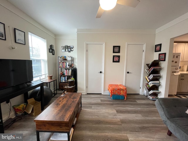 living area featuring crown molding, wood finished floors, baseboards, and ceiling fan