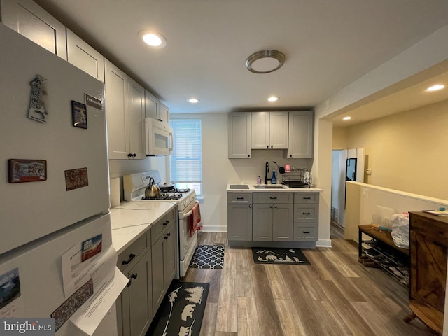 kitchen with a sink, white appliances, dark wood-style flooring, and gray cabinets