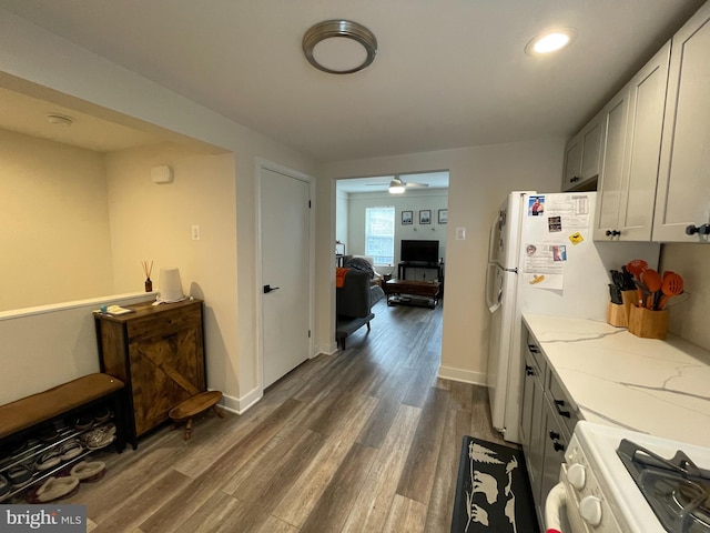 kitchen featuring baseboards, light stone countertops, gas range, freestanding refrigerator, and dark wood-style floors