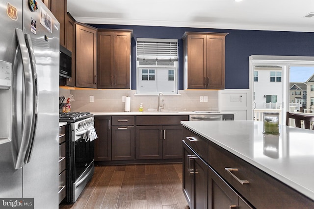 kitchen with a sink, ornamental molding, light countertops, dark wood-type flooring, and stainless steel appliances