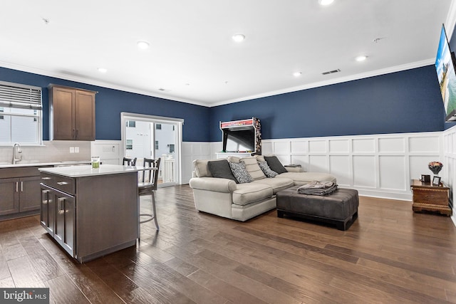 kitchen with a center island, a breakfast bar, dark wood-style flooring, wainscoting, and a sink