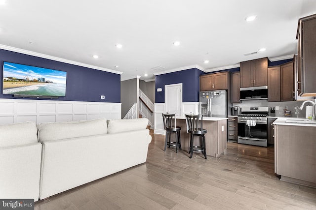 living room with a wainscoted wall, visible vents, ornamental molding, recessed lighting, and light wood-style floors