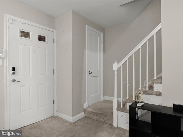 carpeted foyer featuring stairway and baseboards