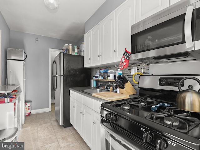 kitchen with a sink, white cabinetry, appliances with stainless steel finishes, decorative backsplash, and baseboards