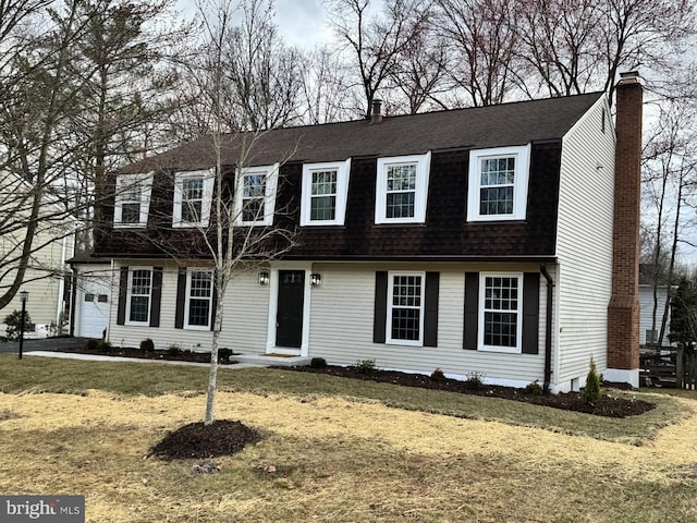 view of front facade with a gambrel roof, a front yard, a chimney, and a shingled roof