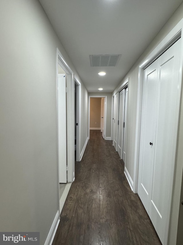 hallway featuring dark wood-type flooring, baseboards, and visible vents